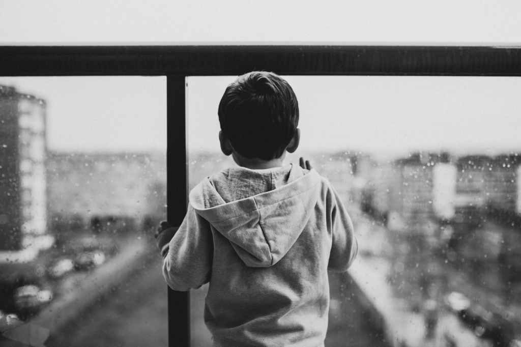A small child looks through balcony glass at a city, black and white photo. Can we not make changes for his sake?